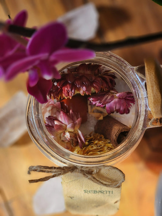 A beautiful glass jar of the Rebirth All-Natural Organic Crystal Bath Soak and natural stone on the inside.
