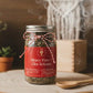 Jar labeled 'Heavy Flow + Clot Release' with a red label on a wooden surface, surrounded by plants and a wooden spoon.