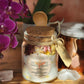 A beautiful glass jar of the Rebirth All-Natural Organic Crystal Bath Soak next to a wooden spoon and quartz crystals