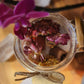 A beautiful glass jar of the Rebirth All-Natural Organic Crystal Bath Soak and natural stone on the inside.
